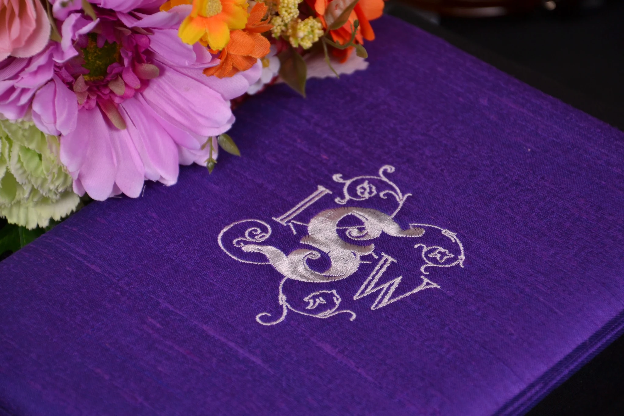 Purple handmade silk wedding invitation box with white custom embroidered monogram and wedding flowers